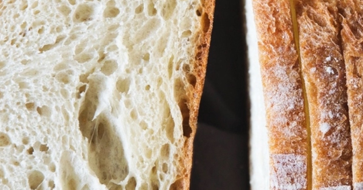 A sliced loaf of white bread on a dark surface, showing the crumb and crust.