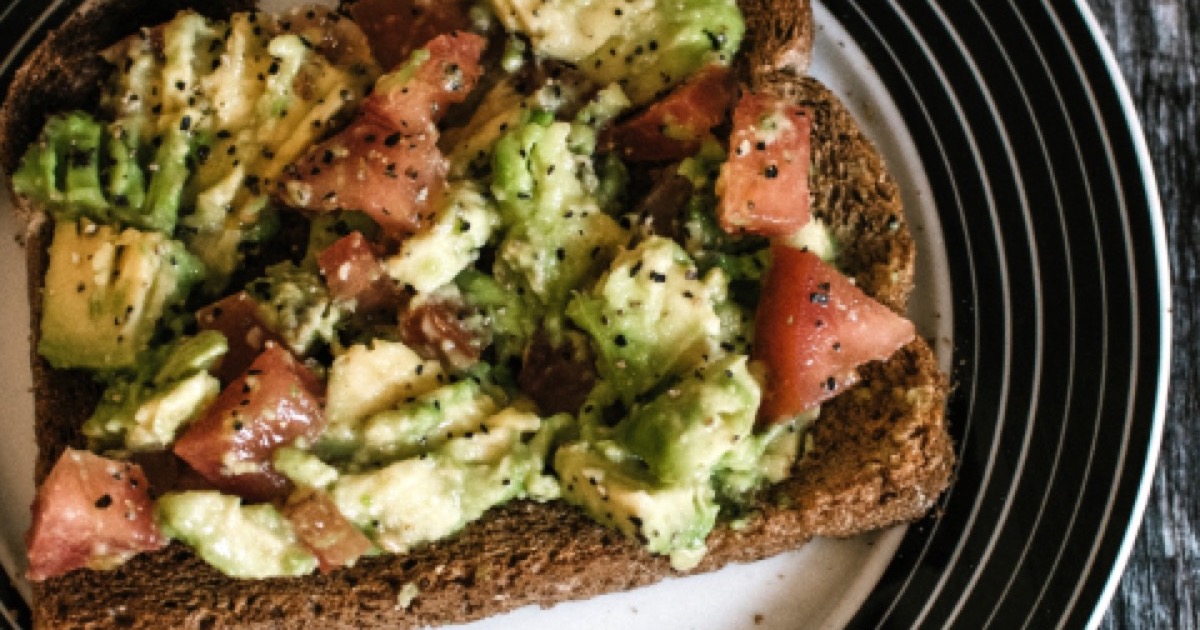 Smashed avocado with chopped tomato on a slice of dark toast, seen from above.
