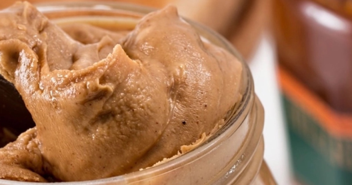 A close-up of a glass jar filled with smooth peanut butter.