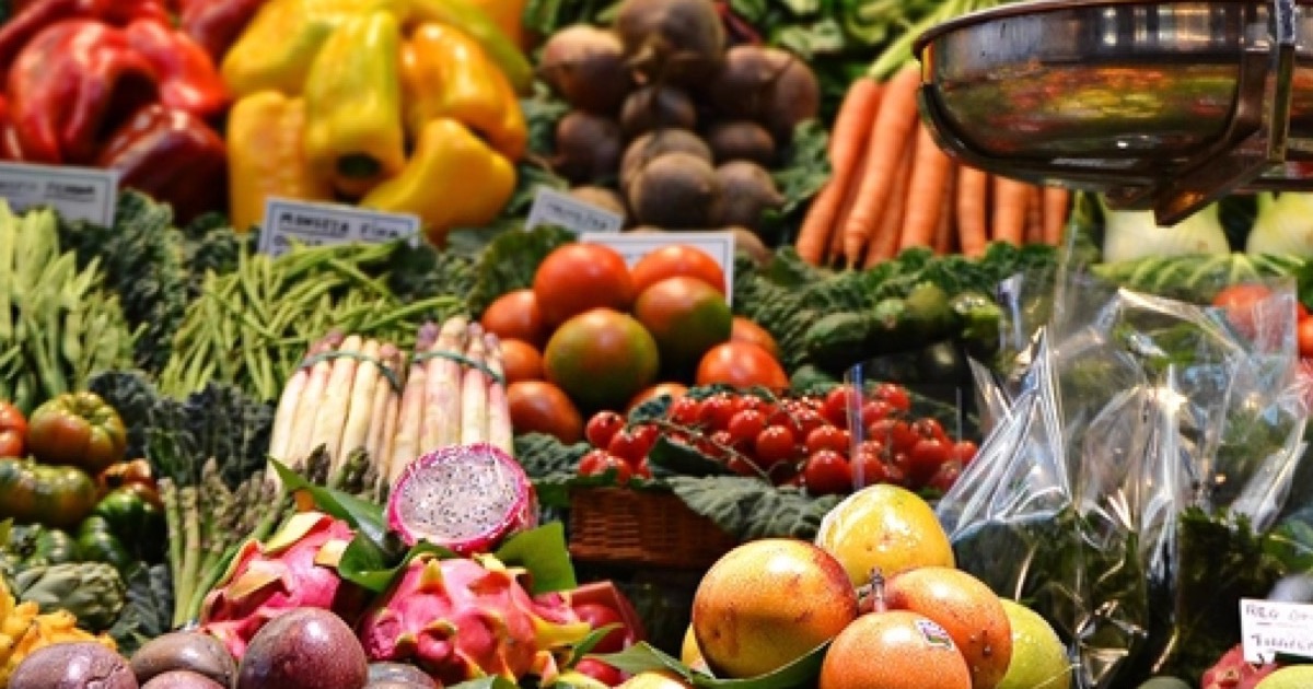 A farmers market stall piled with peppers, carrots, tomatoes, asparagus and fresh fruit.